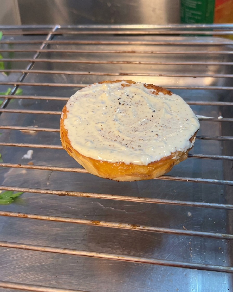 Montage dun burger avec de la roquette, de la tomate et des cornichons sur le pain inférieur.