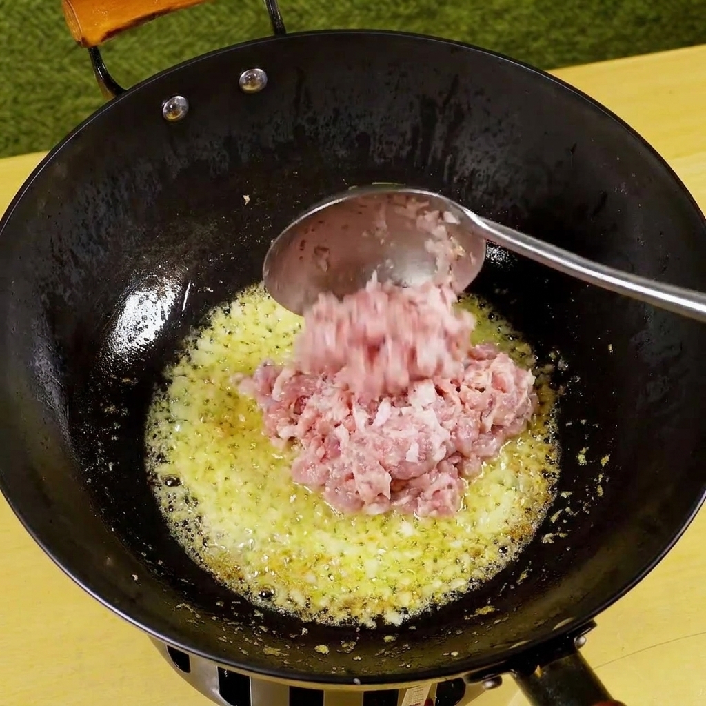 Porc haché ajouté à la poêle avec les oignons et lail, commençant à dorer.