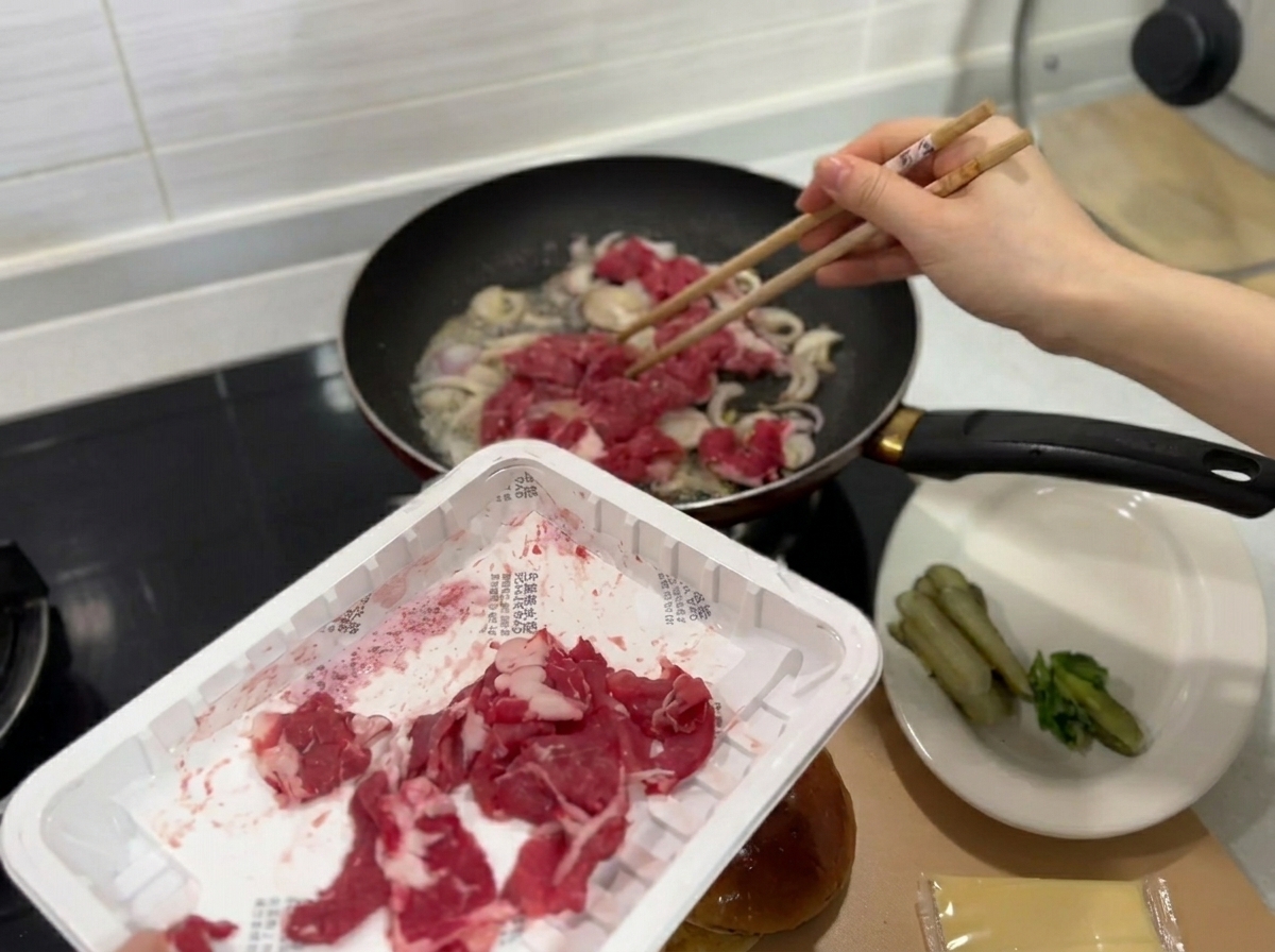 Fines tranches de bœuf cru frais ajoutées dans la poêle contenant les oignons.