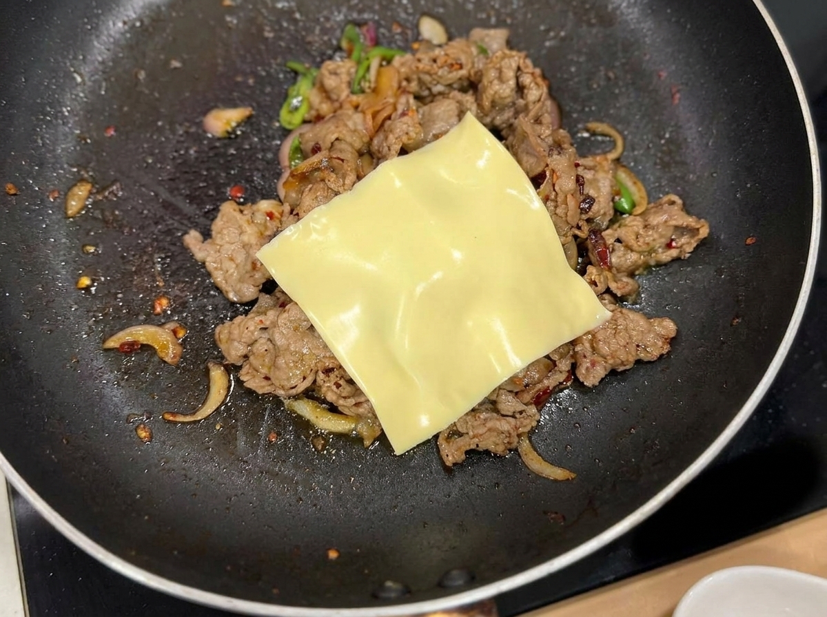 Une tranche de fromage jaune fondant sur le mélange de bœuf et doignon dans la poêle.