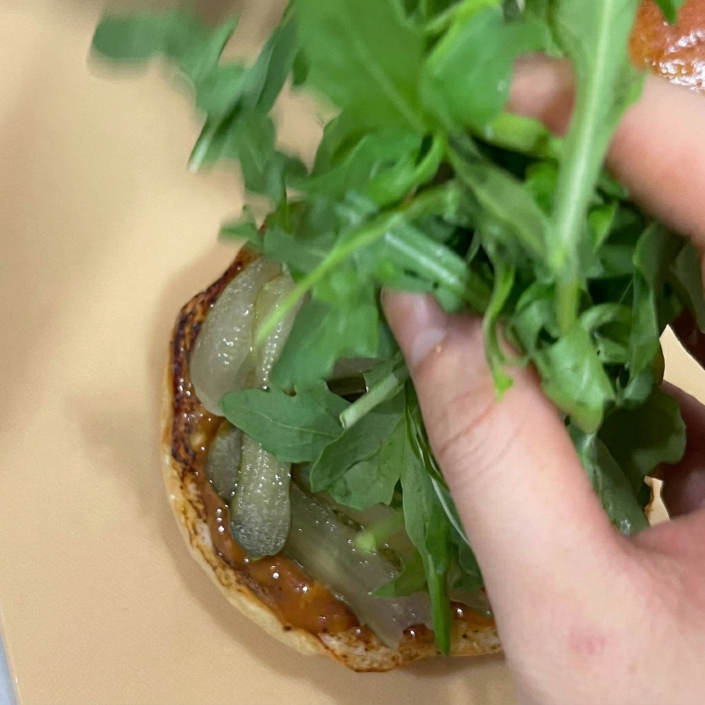 Une main ajoutant une poignée de roquette fraîche sur les cornichons.