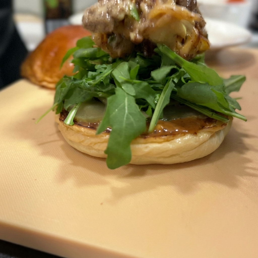 Une épaisse couche de bœuf sauté et doignons rouges surmontée de fromage fondu sur un lit de roquette.