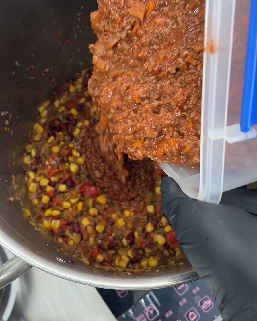 Riche sauce à la viande versée dans une grande marmite remplie de légumes colorés et dépices.