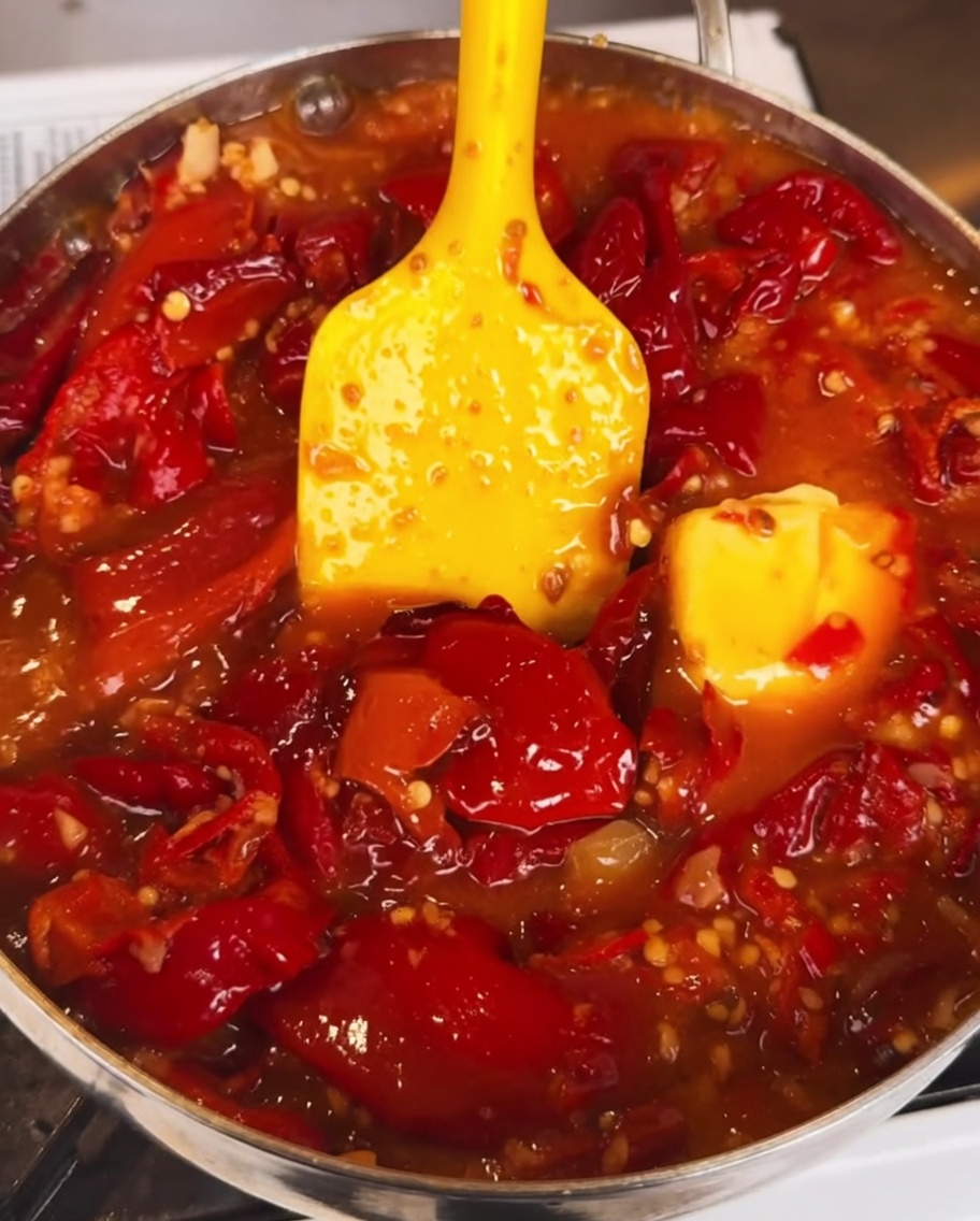 La sauce chili mijotant dans une poêle alors quune sauce sombre et épaisse est ajoutée, créant une finition riche et brillante.