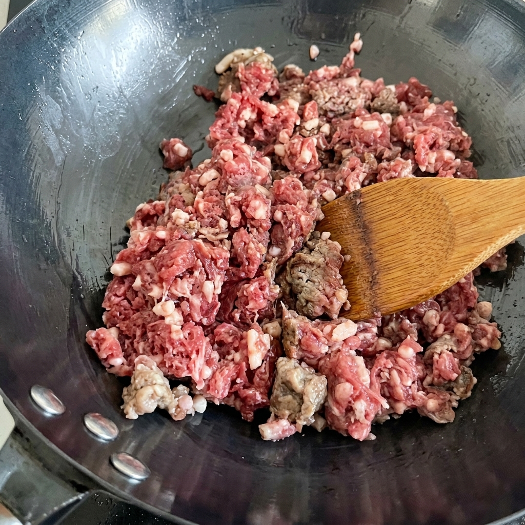 Bœuf haché frais en train de sauter dans un wok chaud, passant de la couleur rouge à brune.