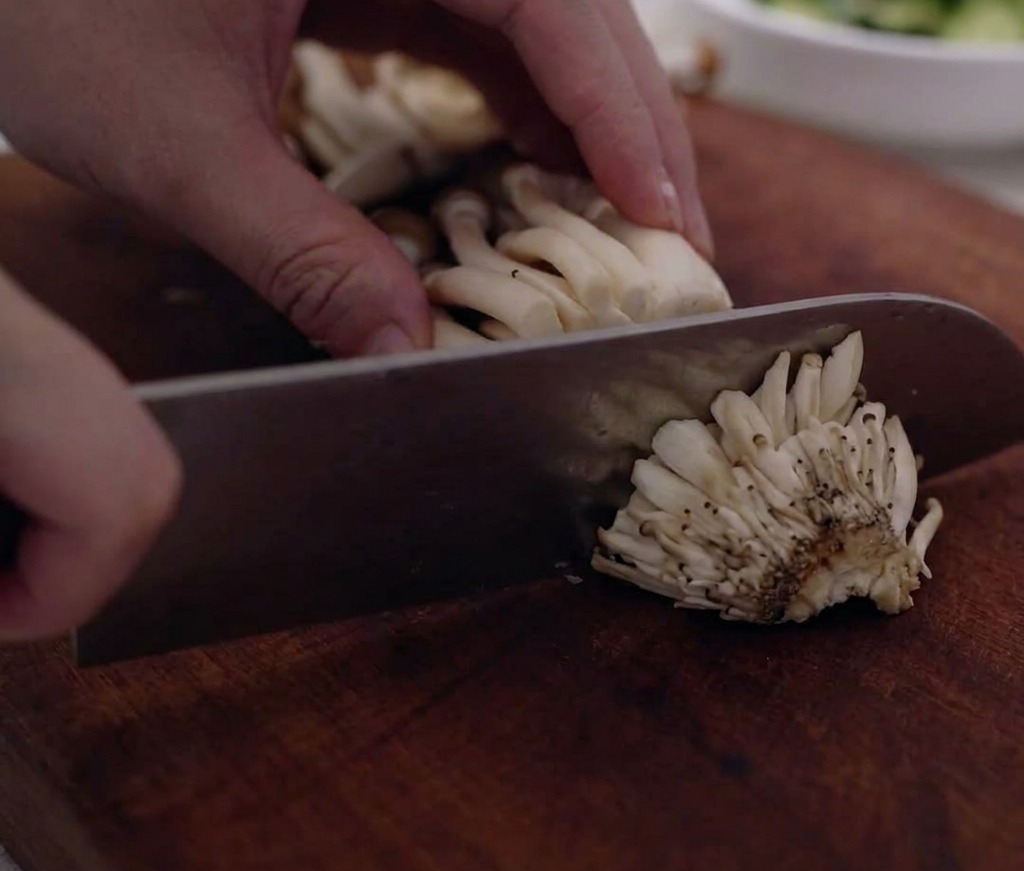Grappes de champignons shimeji dont les bases ligneuses sont retirées sur une planche.