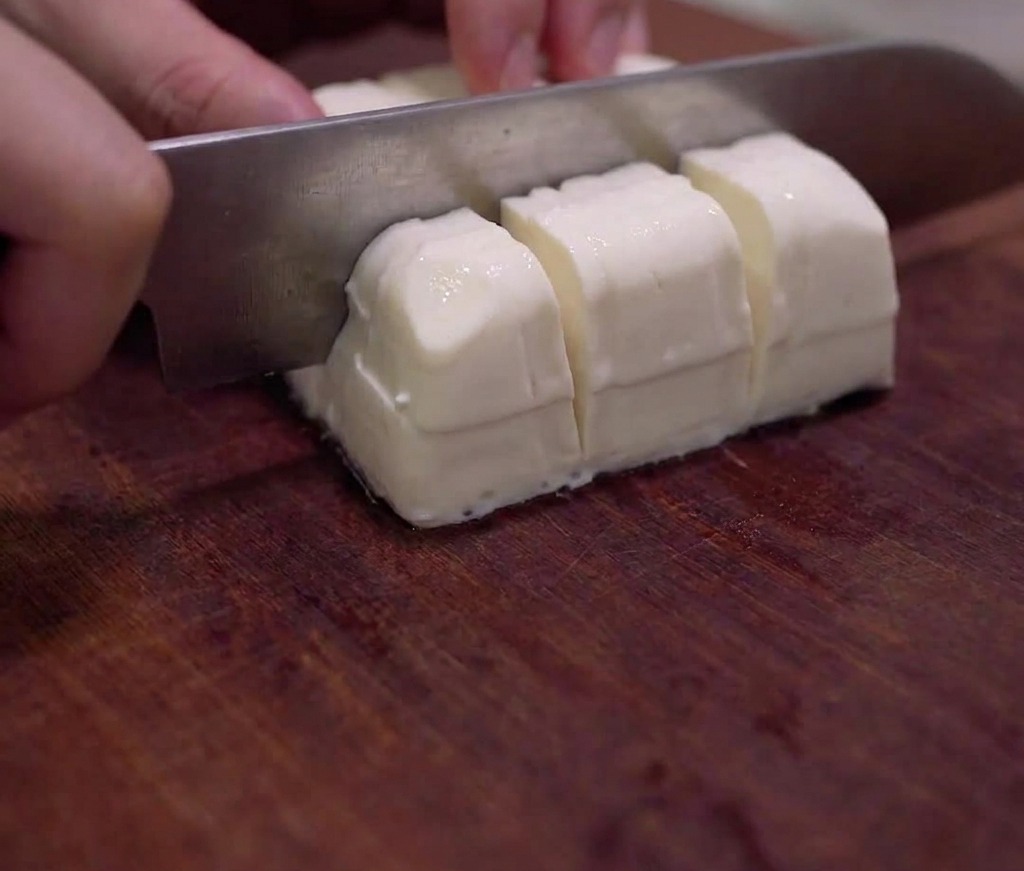 Un bloc de tofu soyeux coupé délicatement en petits cubes sur une planche en bois.