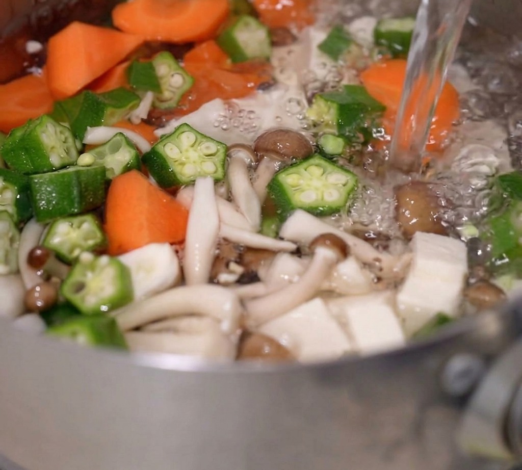 Eau bouillante versée dans une casserole contenant les légumes et le tofu.