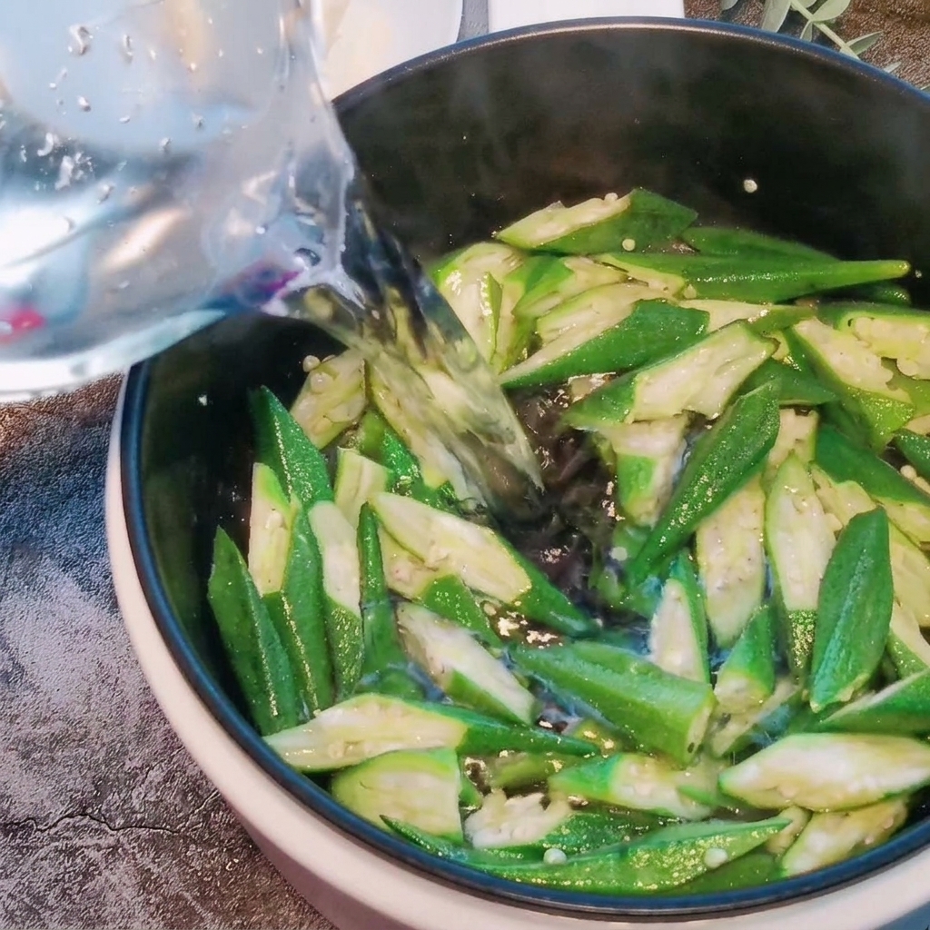Eau versée dans une marmite contenant les morceaux de gombo sautés.