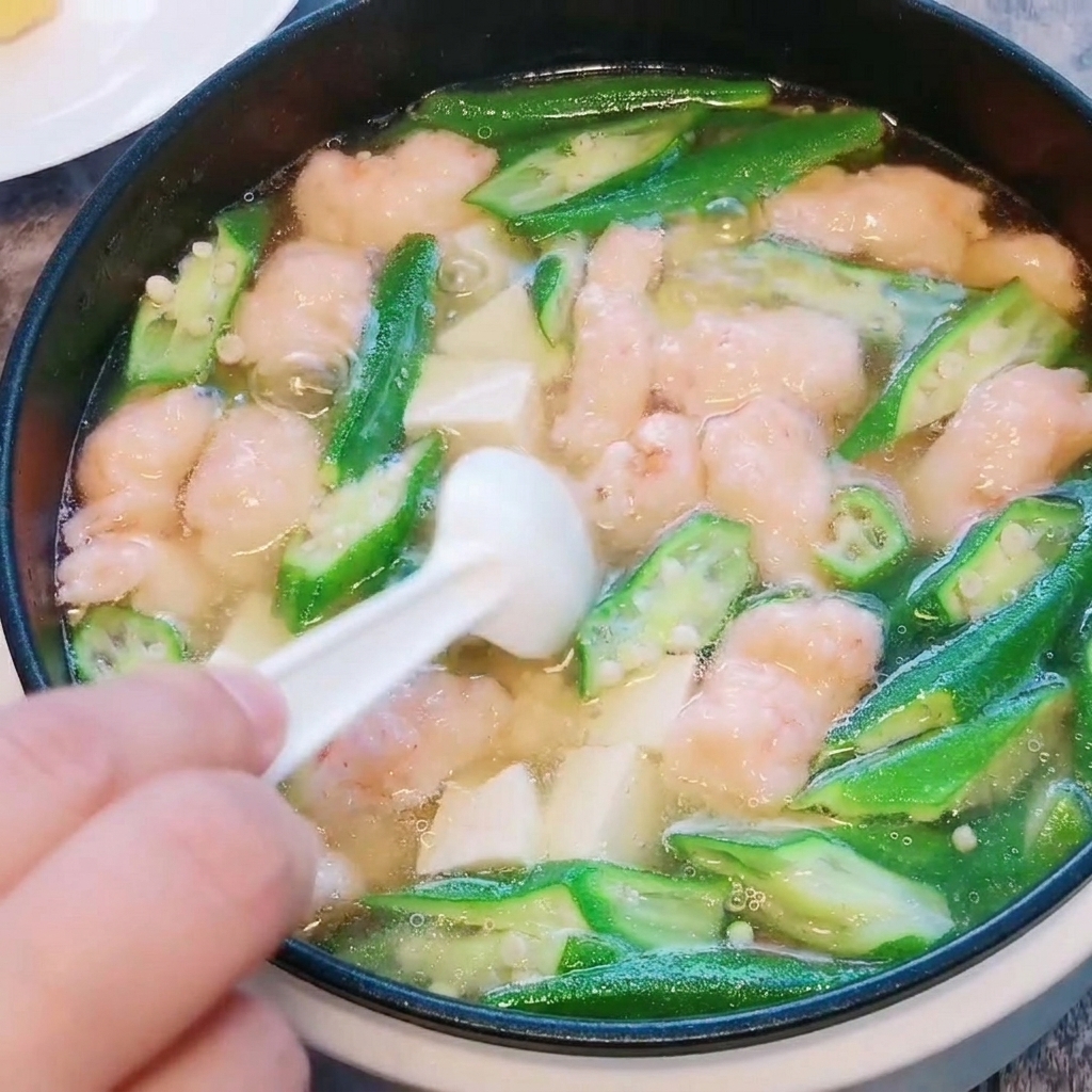 Gros plan sur du sel et du poivre blanc saupoudrés dans la soupe de gombo, tofu et pâte de crevettes terminée.