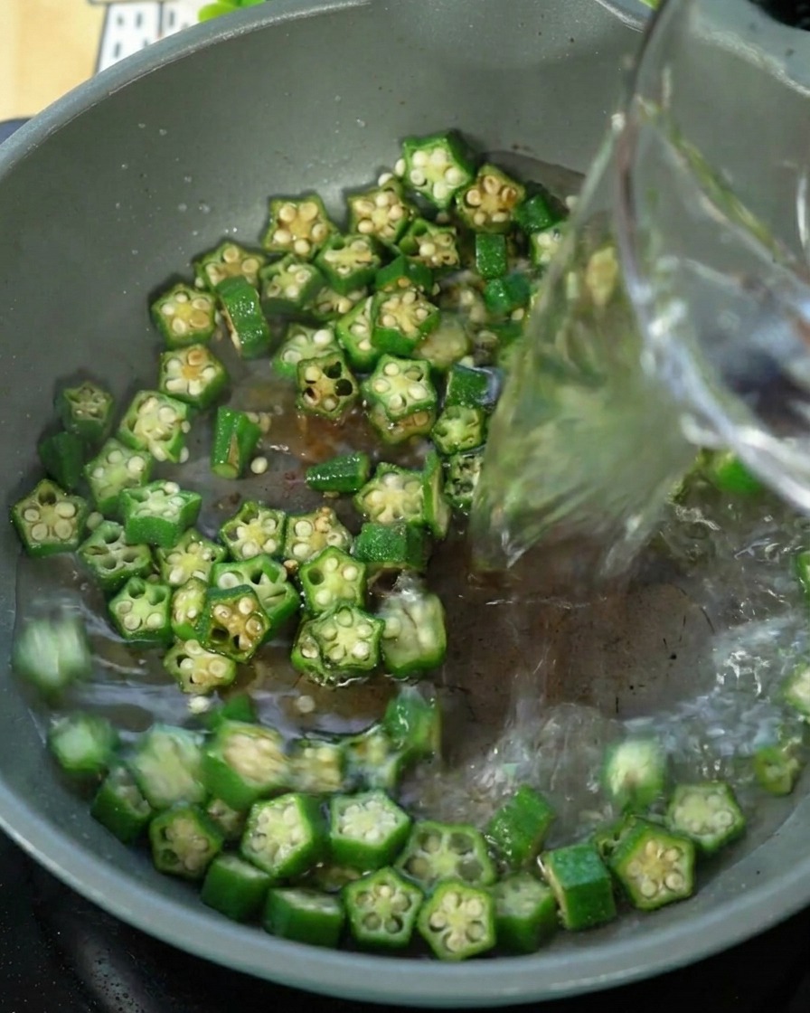 Eau versée dans une poêle contenant le gombo sauté.