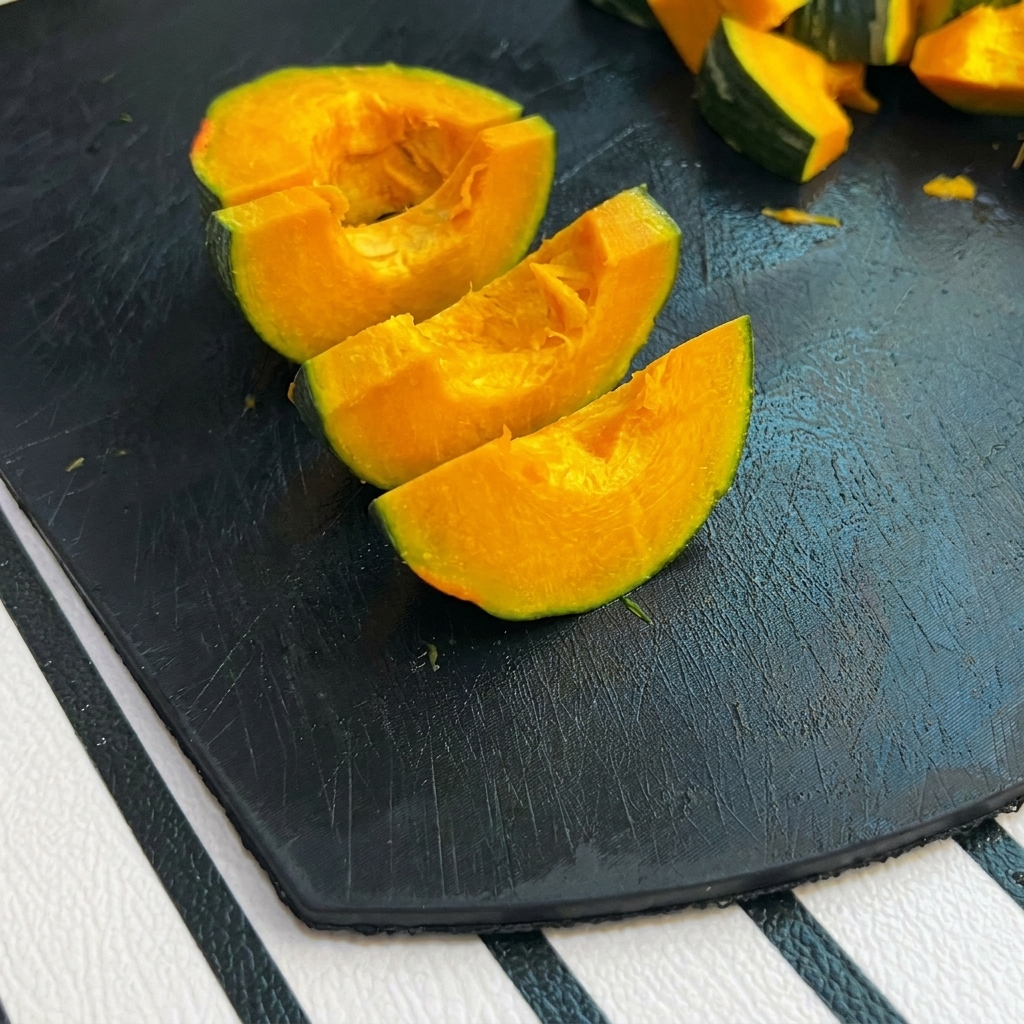 Petits morceaux de potiron à peau verte sur une planche à découper noire.