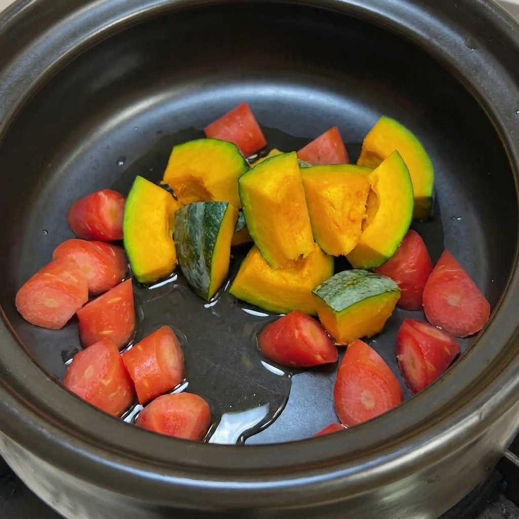 Une marmite en argile noire contenant des morceaux de potiron à peau verte et des carottes orange vif brillant avec de lhuile avant dêtre sautés.
