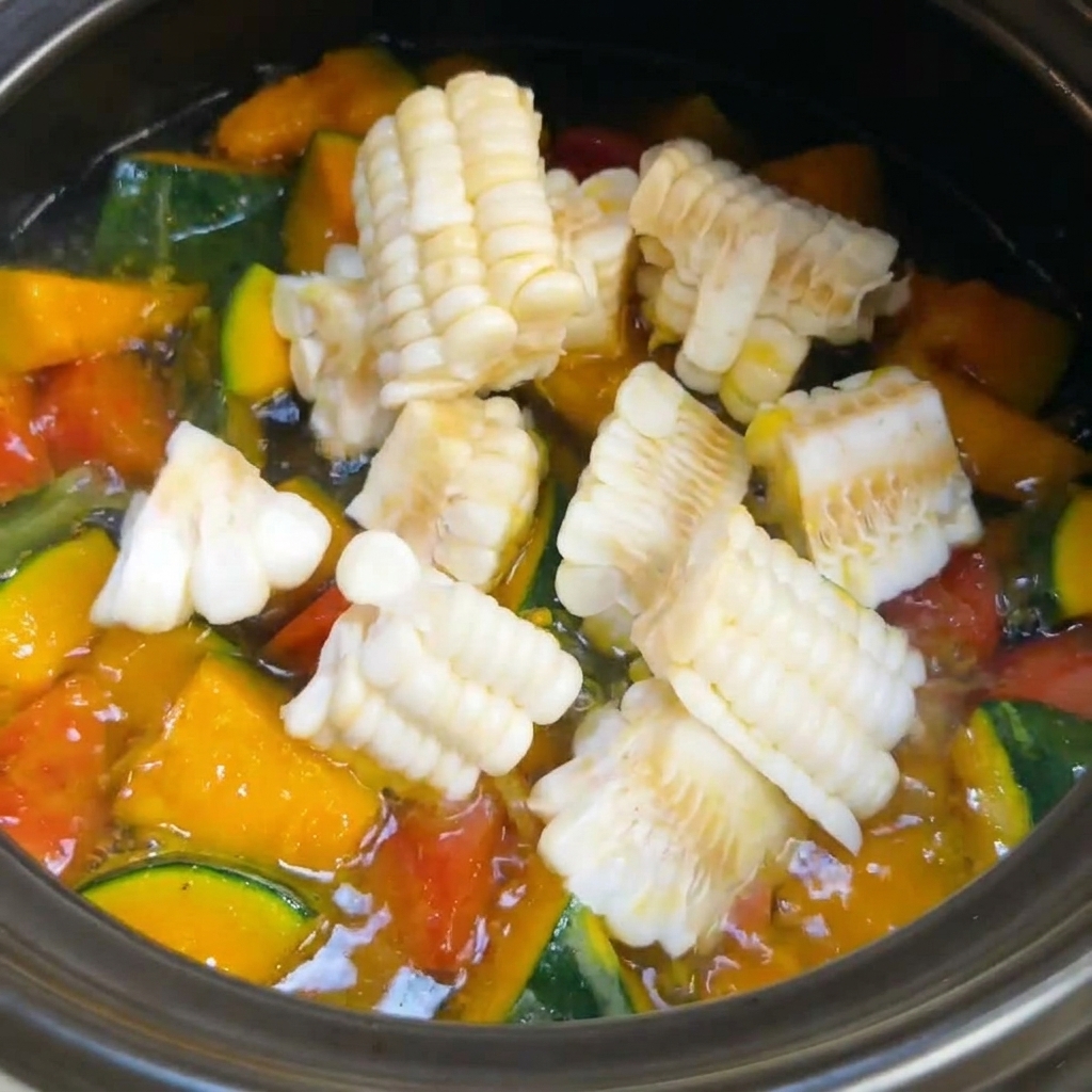 Des segments de maïs fraîchement coupés ajoutés dans une marmite de soupe aux légumes bouillonnante.