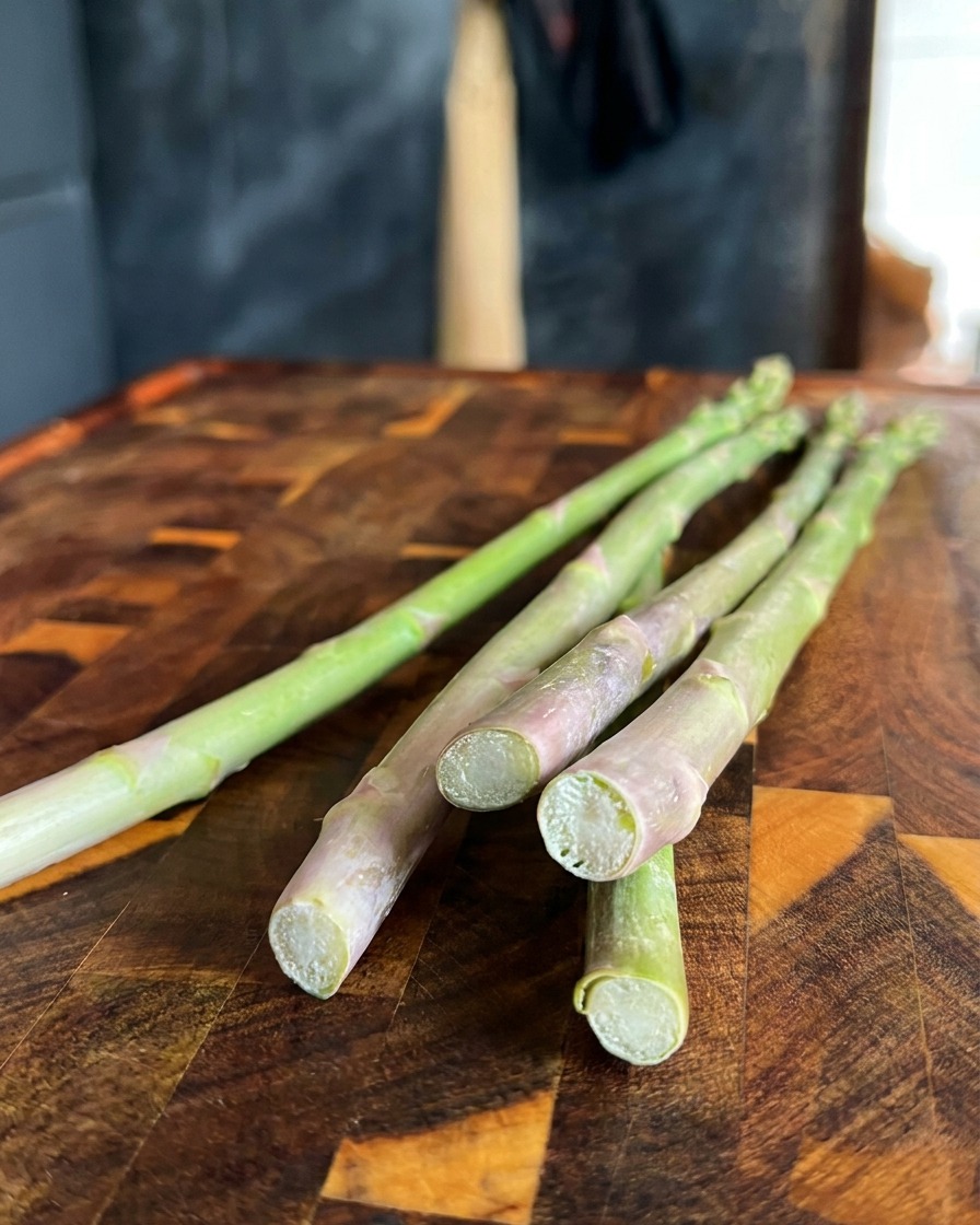 Gros plan sur des asperges vertes fraîches dont on coupe les pieds fibreux sur une planche en bois.