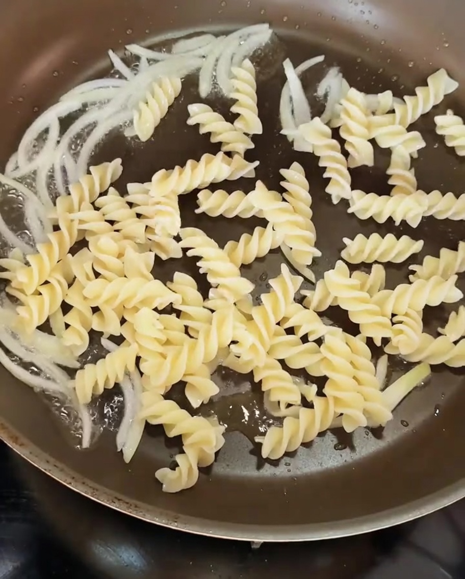 Pâtes torsadées cuites ajoutées dans la poêle contenant les oignons sautés.