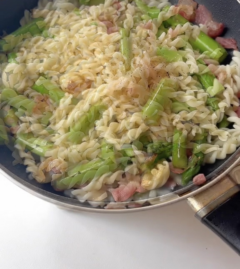 Poivre noir saupoudré sur le mélange de pâtes, dasperges et de bacon.