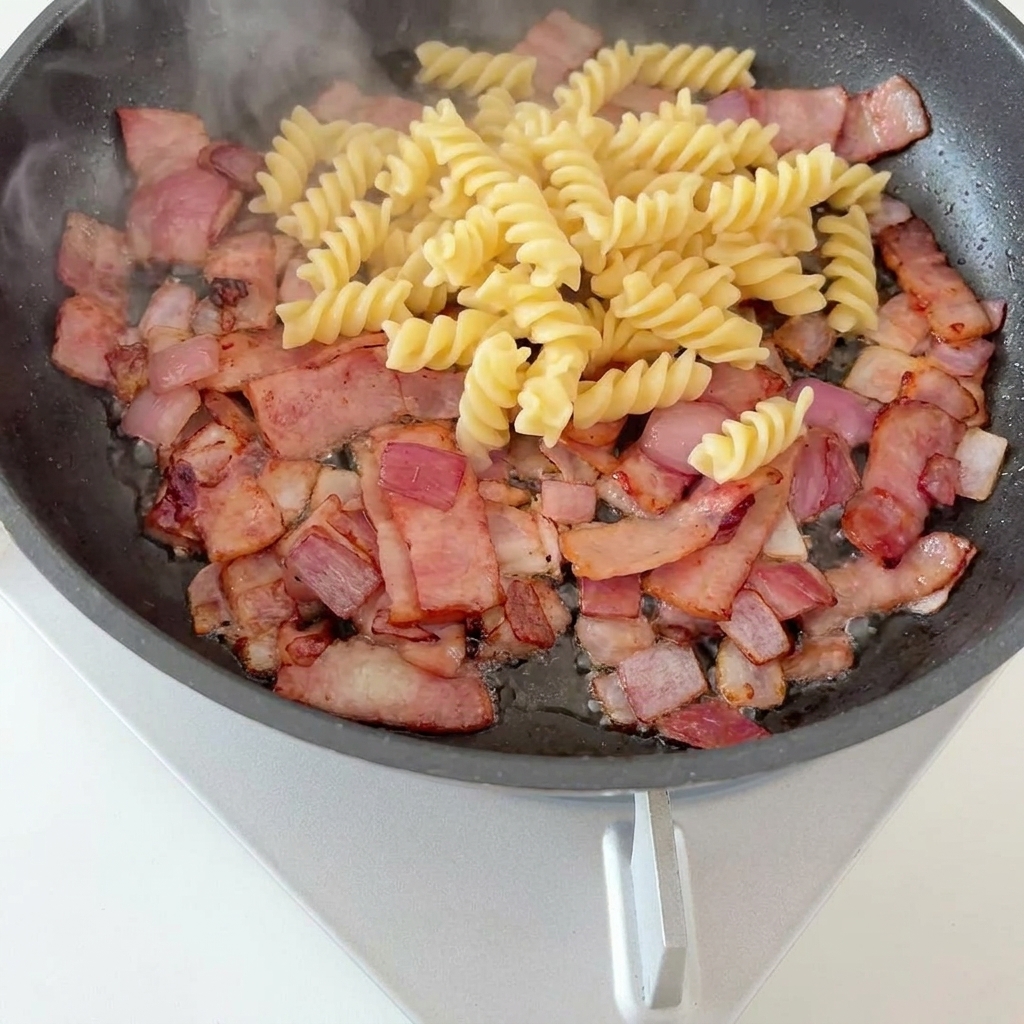 Fusilli et asperges disposées sur une base de bacon croustillant et oignons caramélisés.