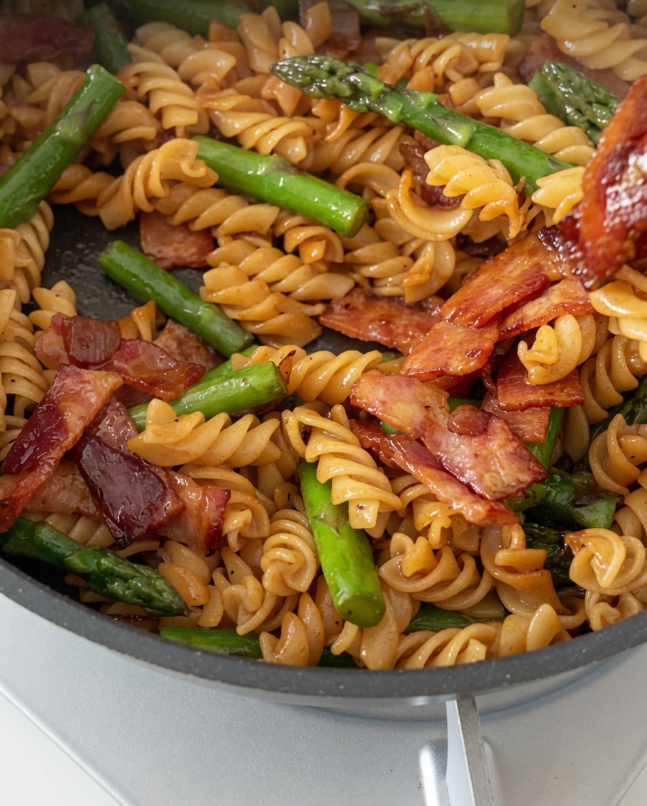 Fusilli, bacon et asperges enrobés dune sauce brillante dans une poêle.