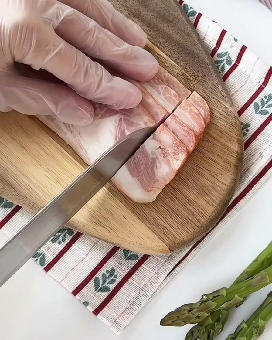 Tranches de bacon cru coupées en petits carrés uniformes sur une planche à découper en bois.