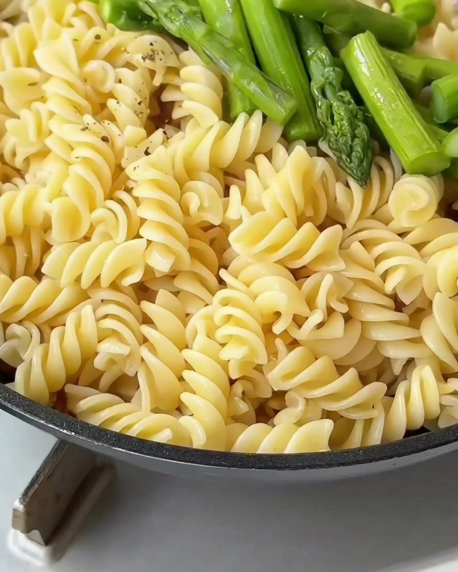 Pâtes fusilli et asperges vertes dans une poêle assaisonnées de poivre noir concassé.