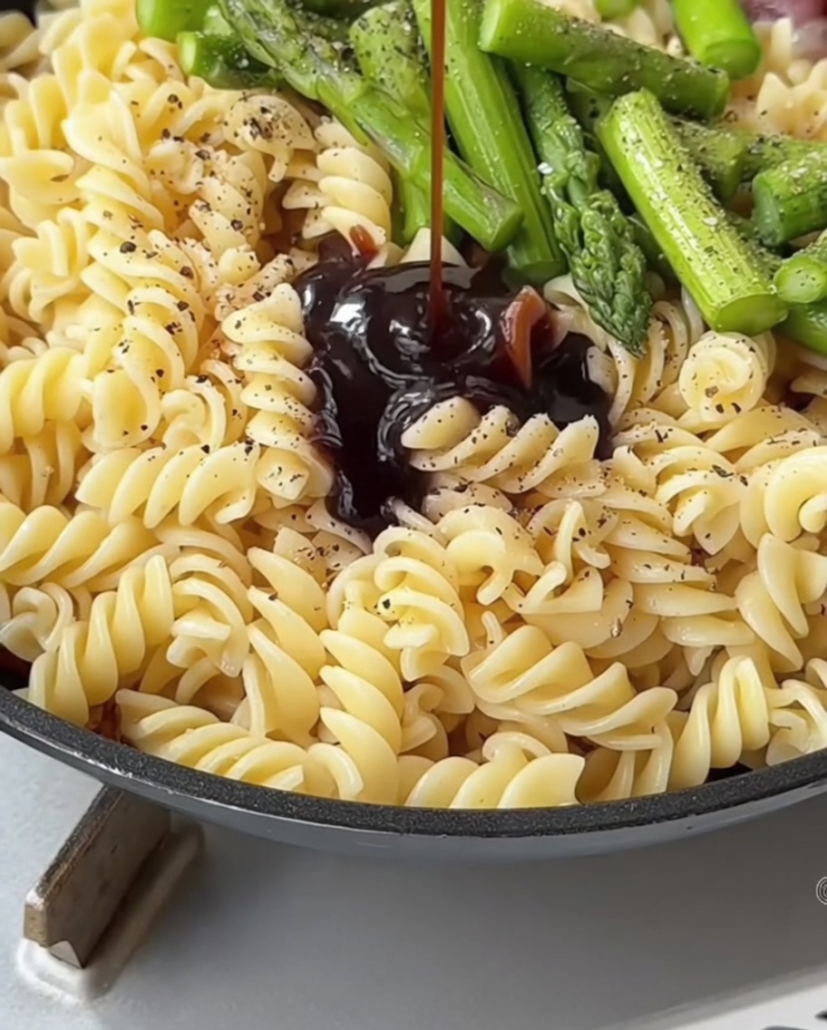 Un mélange de sauce savoureuse versé à la cuillère sur les pâtes et les asperges dans une poêle.