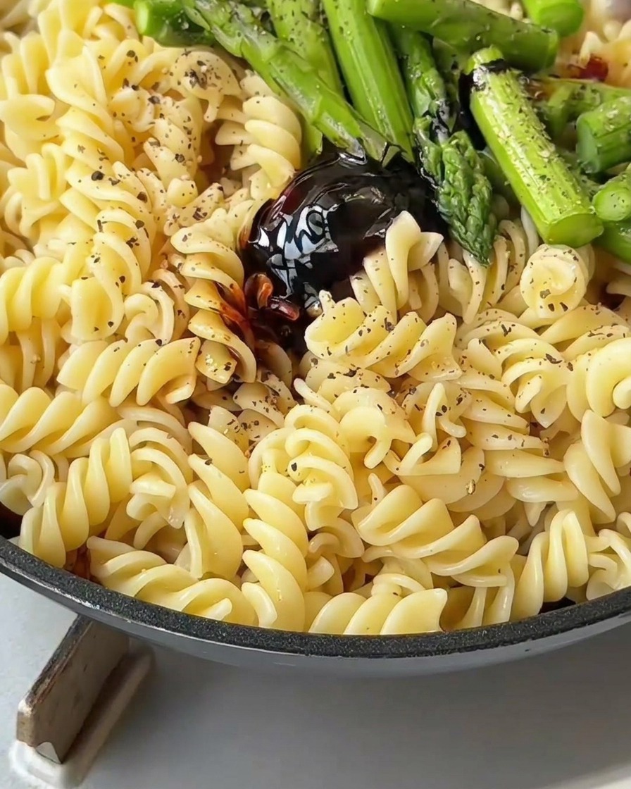 Pâtes, bacon et asperges mélangés avec une spatule dans une poêle pour les enrober de sauce.