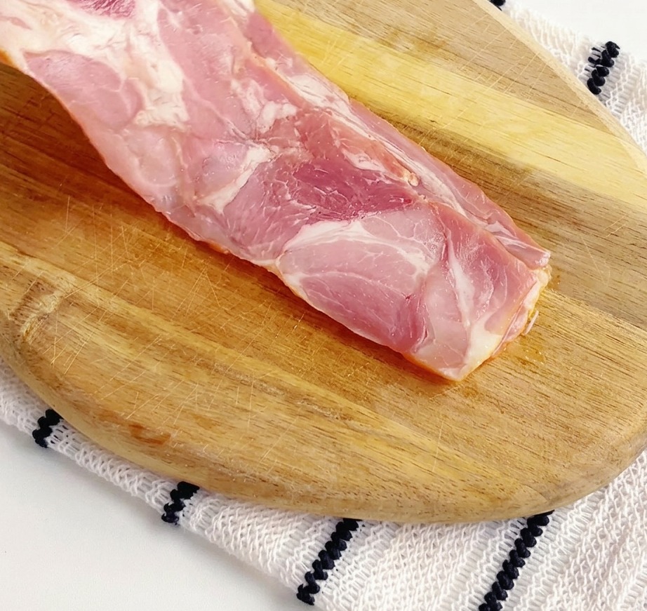 Tranches de bacon cru coupées en petits morceaux sur une planche à découper en bois.