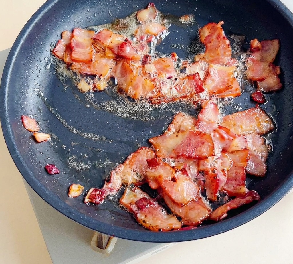 Morceaux de bacon en train de frire dans une poêle avec des oignons jusquà ce quils soient dorés et croustillants.