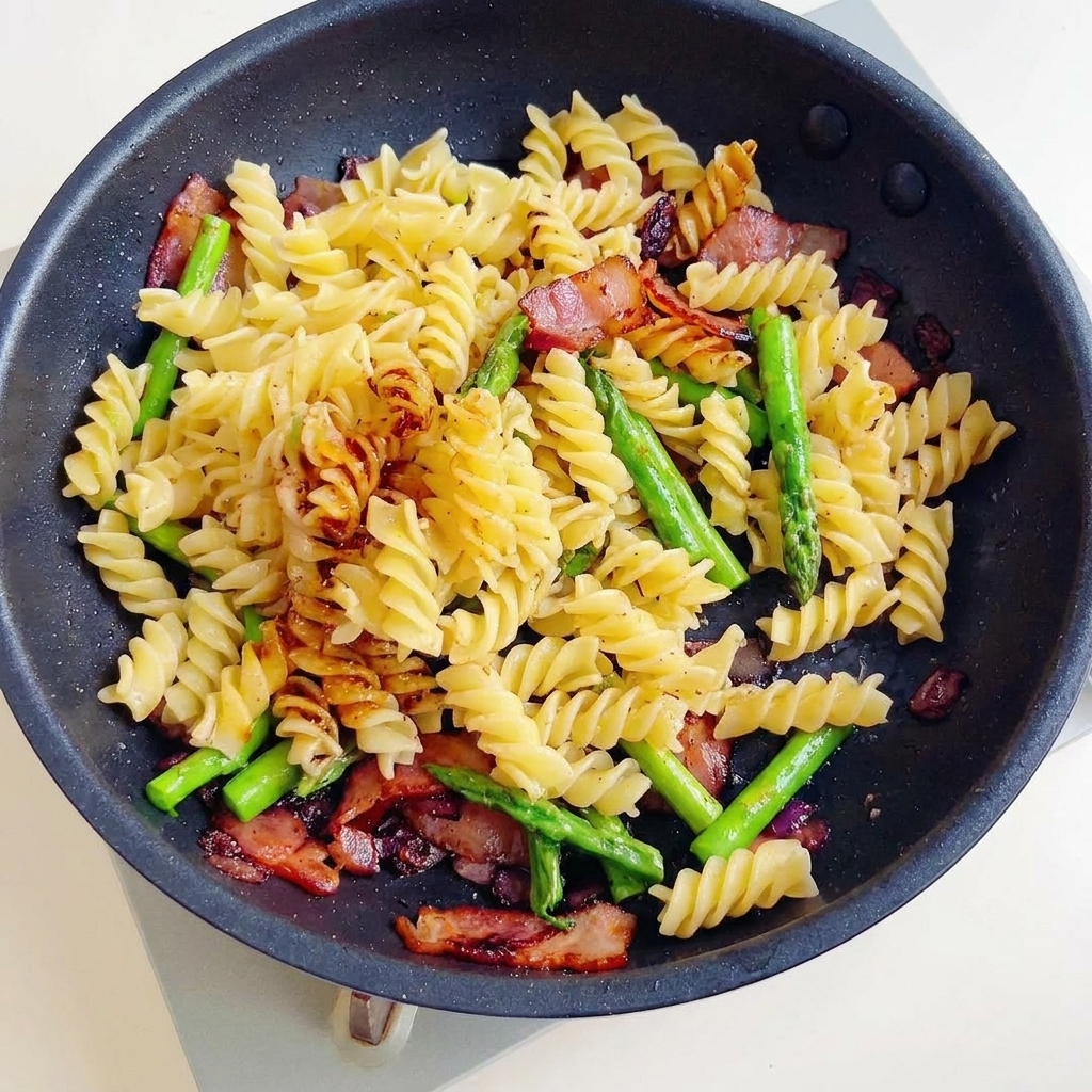 Un délicieux sauté de fusillis, bacon croustillant et asperges mélangé dans une sauce sombre et savoureuse dans une poêle.