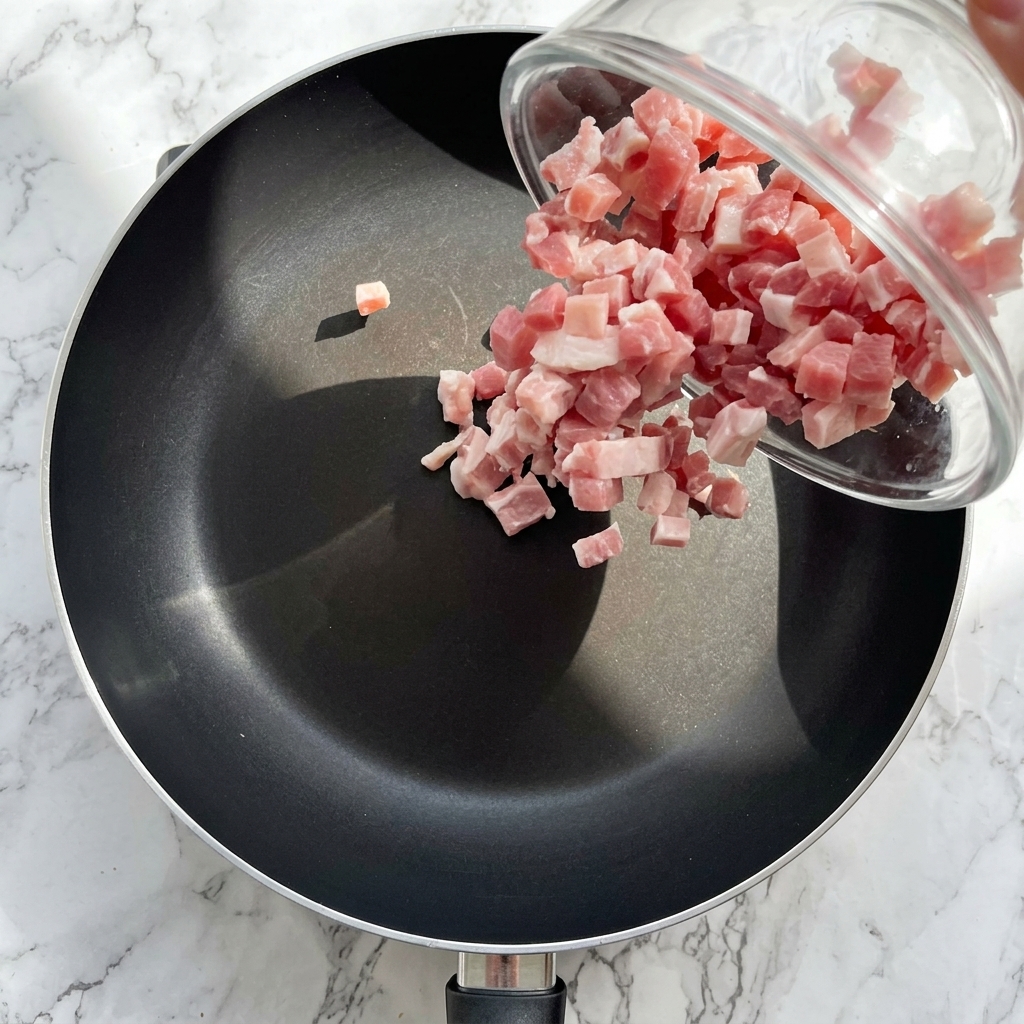 Dés de bacon en train de dorer dans une poêle jusquà devenir croustillants.