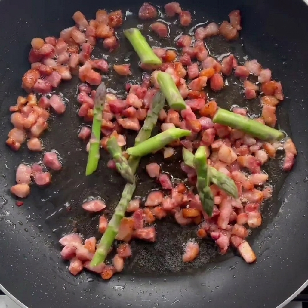 Morceaux dasperges cuisant dans une poêle avec le bacon doré.
