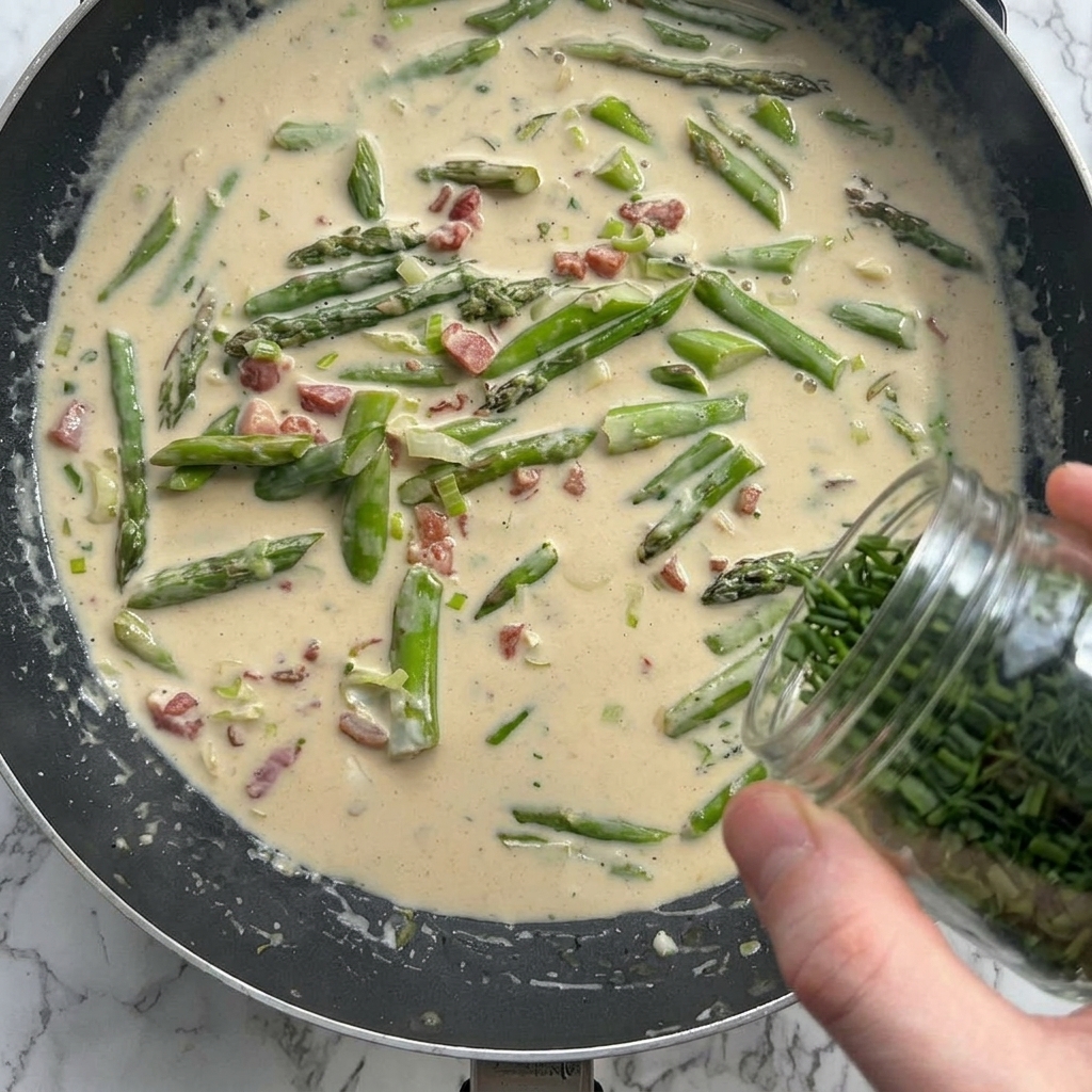 Parmesan et herbes ajoutés à la sauce crémeuse dans la poêle.