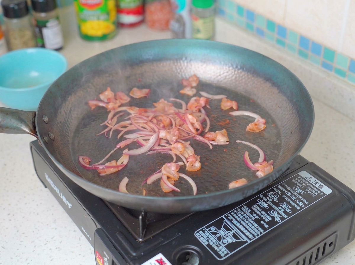 Lamelles doignons et champignons cuisant avec le bacon dans la poêle.