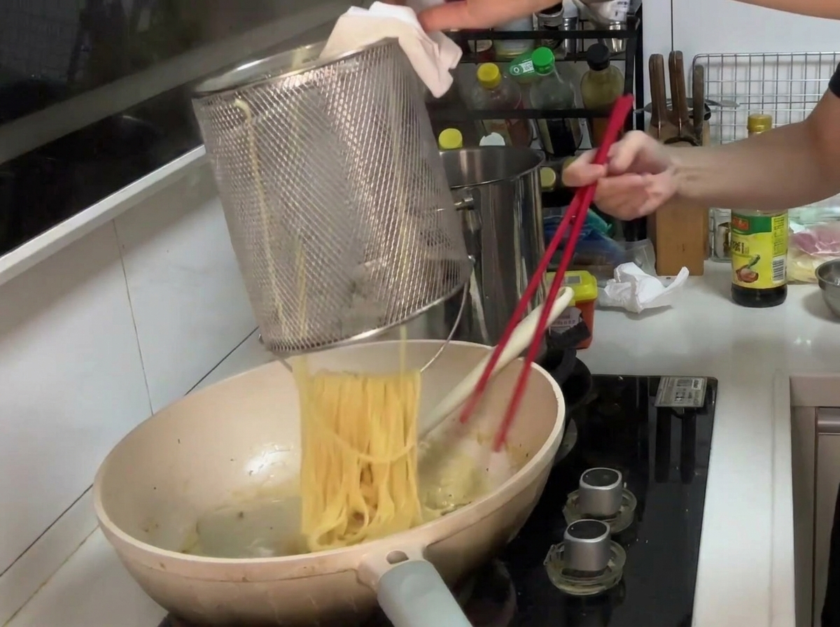 Pâtes transférées dune passoire dans une poêle contenant la sauce crémeuse aux champignons, prêtes à être mélangées.