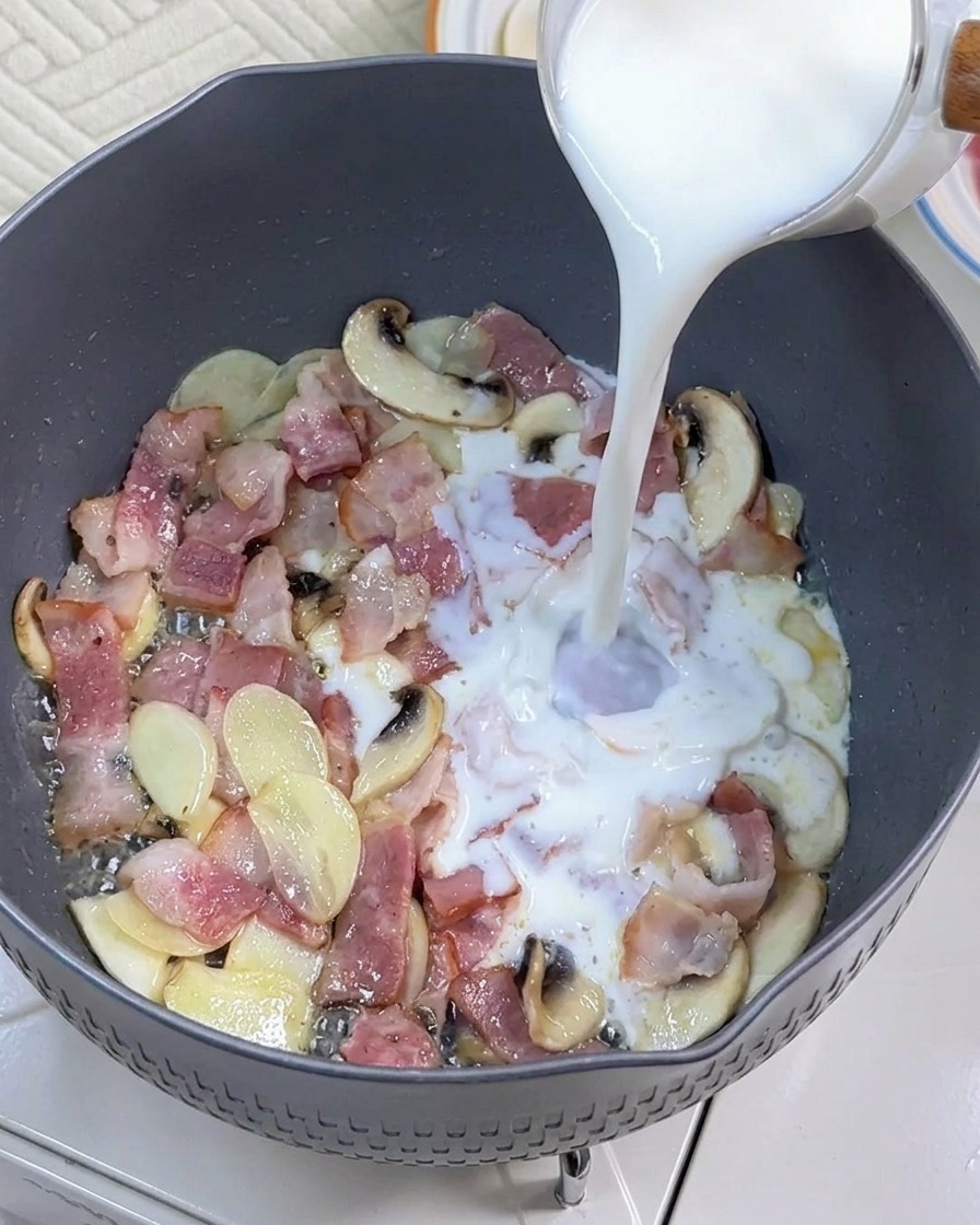 Du lait versé dans une poêle avec le bacon et les champignons sautés.