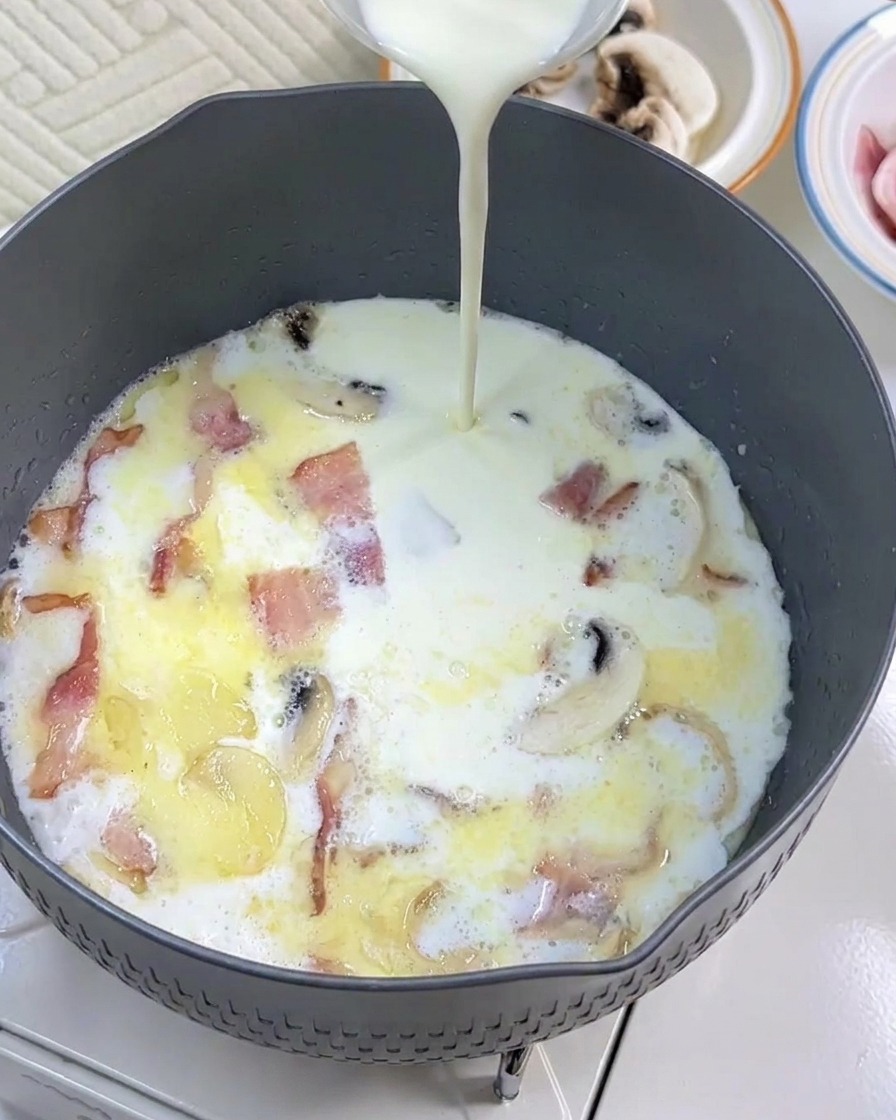 De la crème liquide ajoutée dans la poêle avec le lait, le bacon et les champignons.