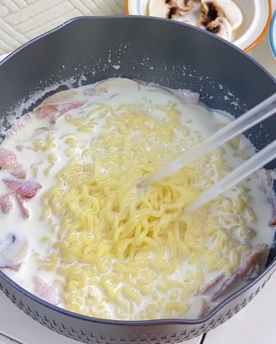 Des nouilles ramen incorporées dans la sauce crémeuse à laide de baguettes.