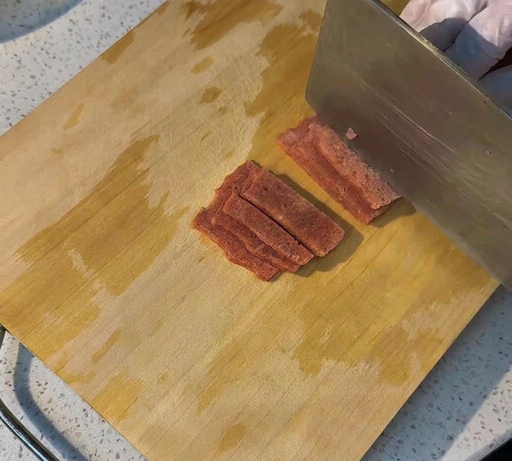 Tranches de bacon cru disposées proprement sur une planche en bois, prêtes à être cuites.
