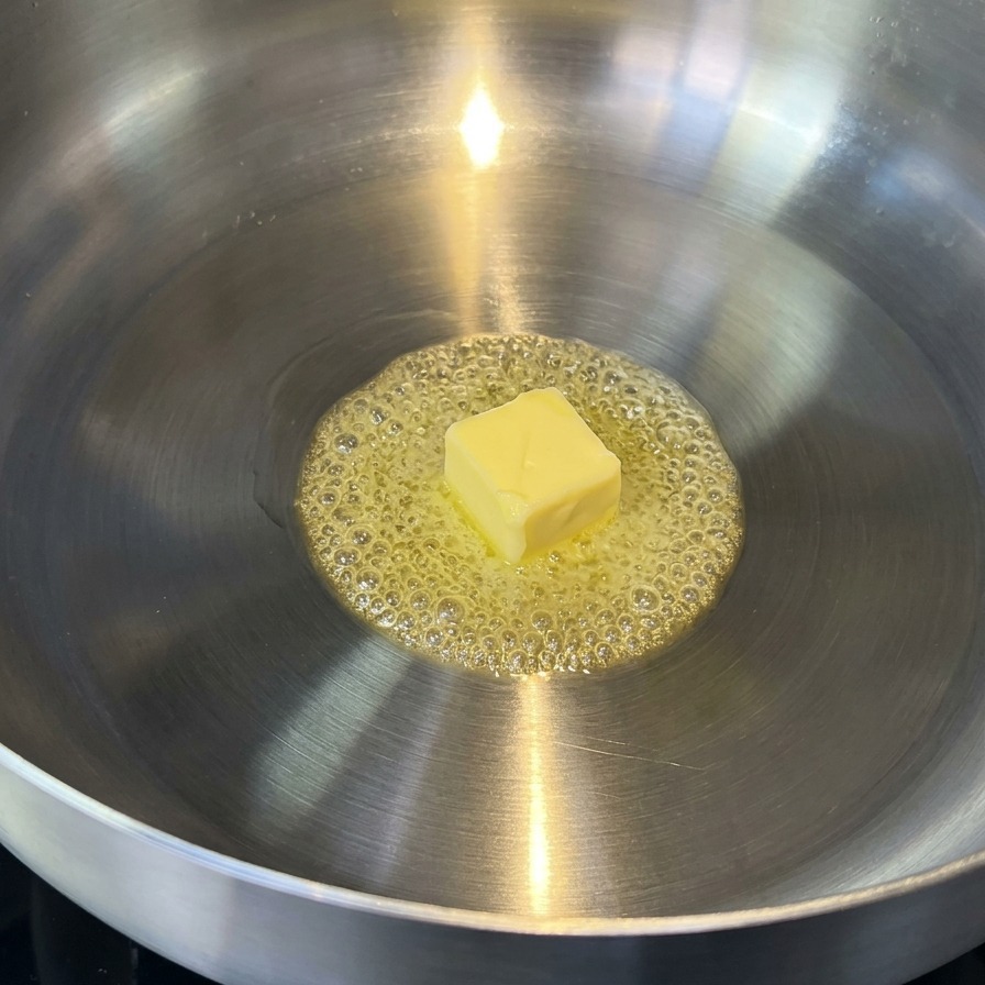Du beurre fondant dans une poêle en inox, formant de petites bulles dorées.