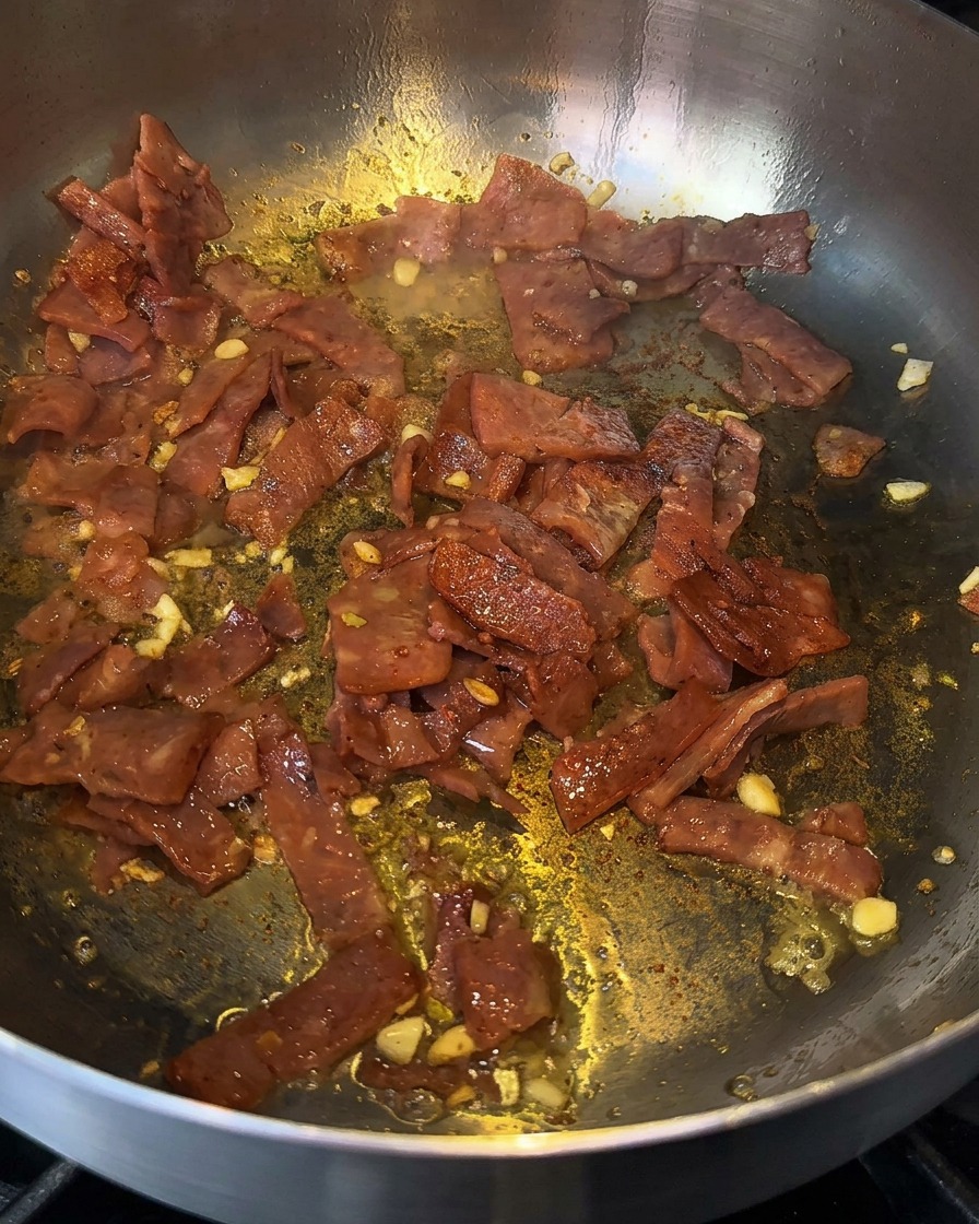 Bacon et ail grésillants dans une poêle, déglacés avec un trait dalcool de cuisine.