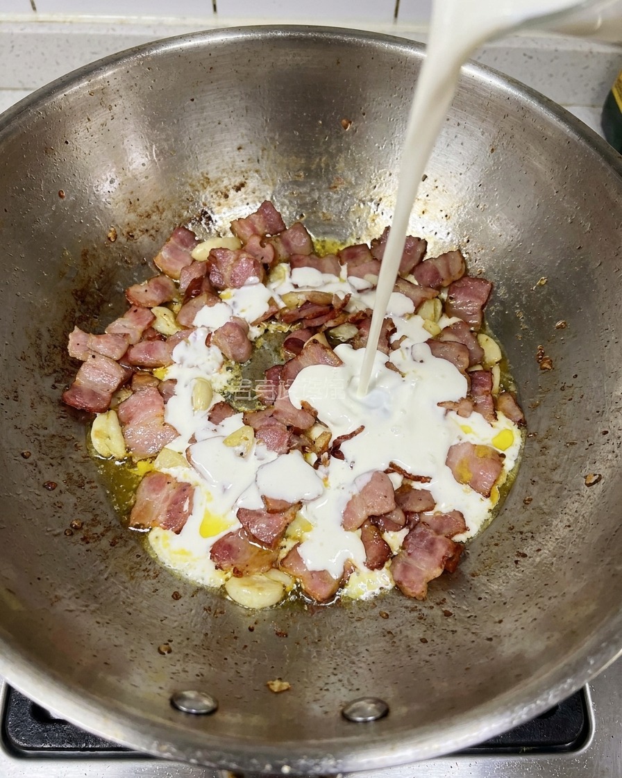 De la crème liquide versée dans une poêle contenant le bacon doré et lail.