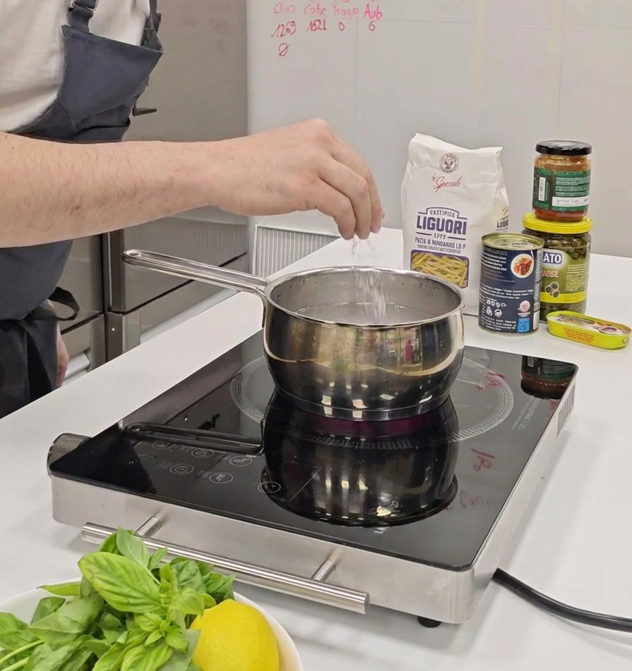 La main dune personne saupoudrant une pincée de sel dans une casserole deau sur une plaque à induction.