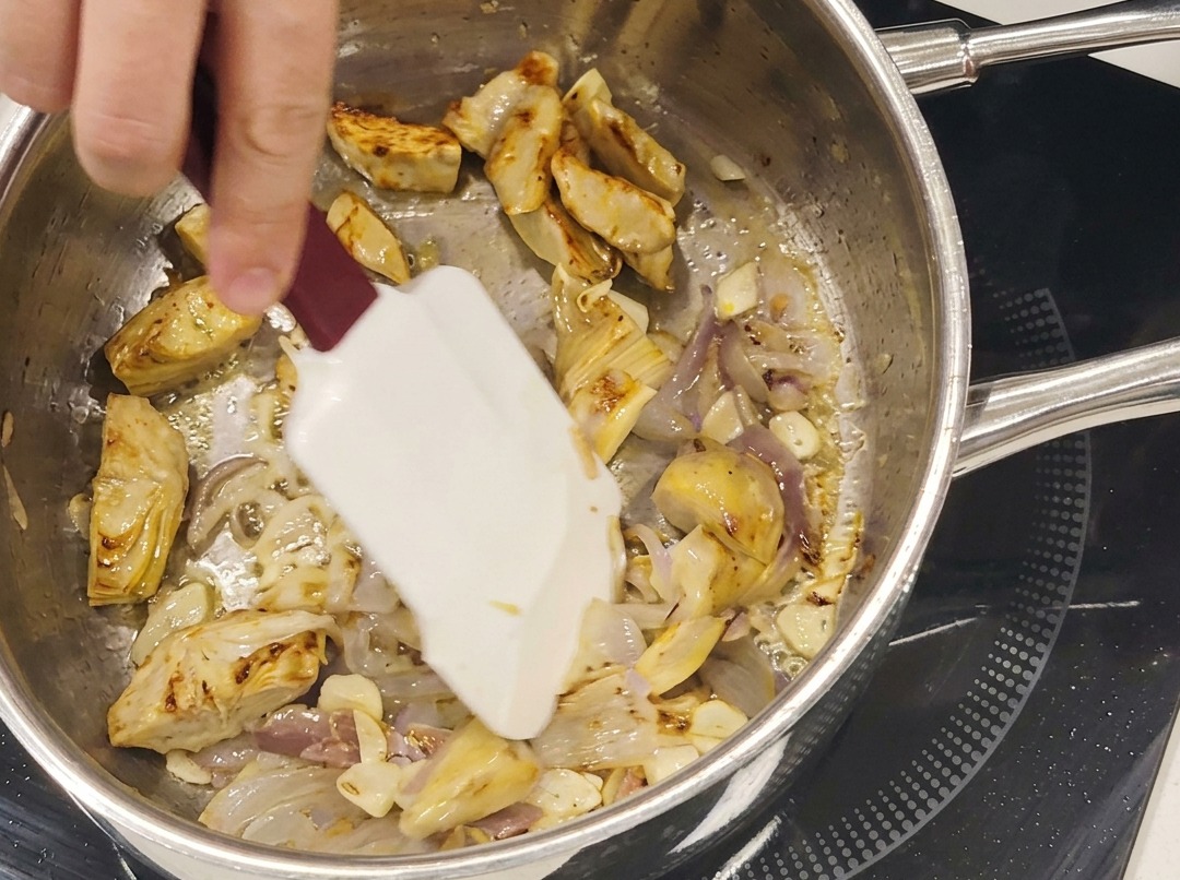 Cœurs dartichauts sautés, lamelles dail et anchois cuisant ensemble dans une poêle en acier inoxydable.