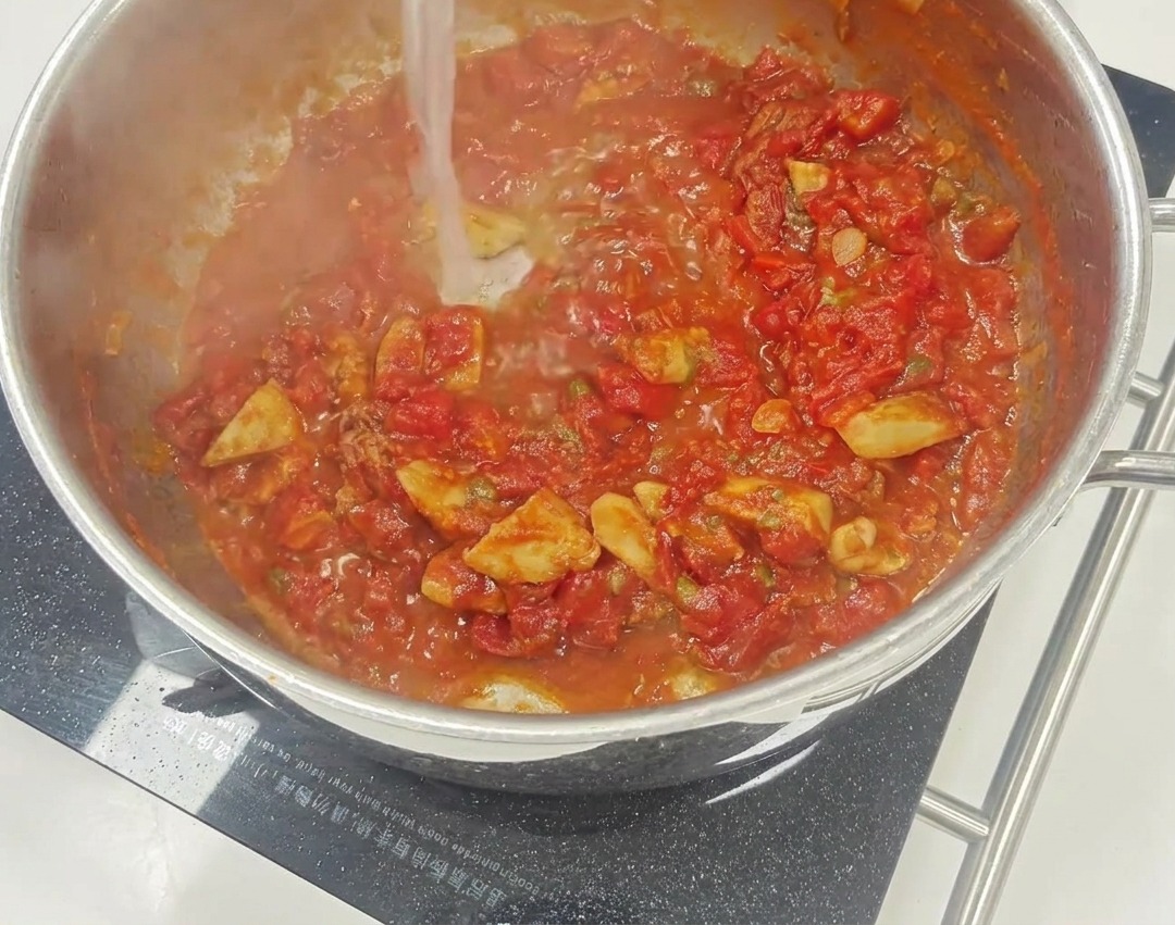 Une sauce tomate rouge vibrante mijotant dans une poêle avec des morceaux visibles de tomates séchées et de câpres.
