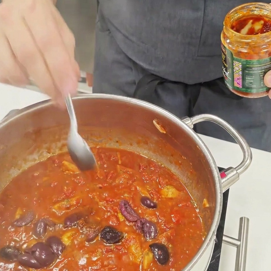 Une cuillerée de sauce pimentée incorporée dans une sauce pour pâtes à base de tomates bouillonnante.