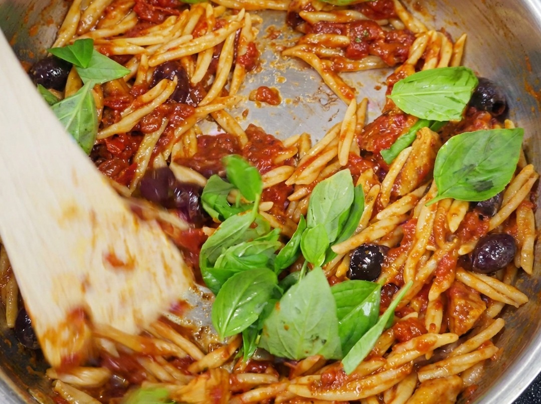 Pâtes Trofie finies, mélangées à la sauce Puttanesca et garnies de feuilles de basilic vert frais.