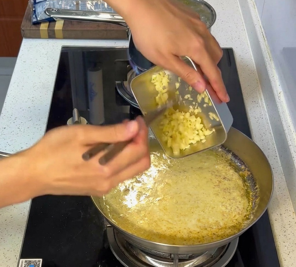 Ail haché incorporé dans une sauce blanche crémeuse dans une poêle en inox.
