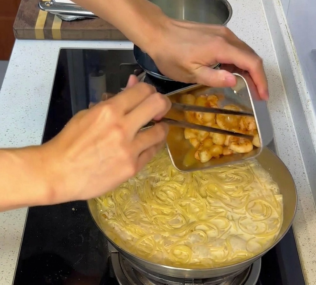 Fruits de mer poêlés ajoutés dans la poêle avec les pâtes crémeuses mélangées.