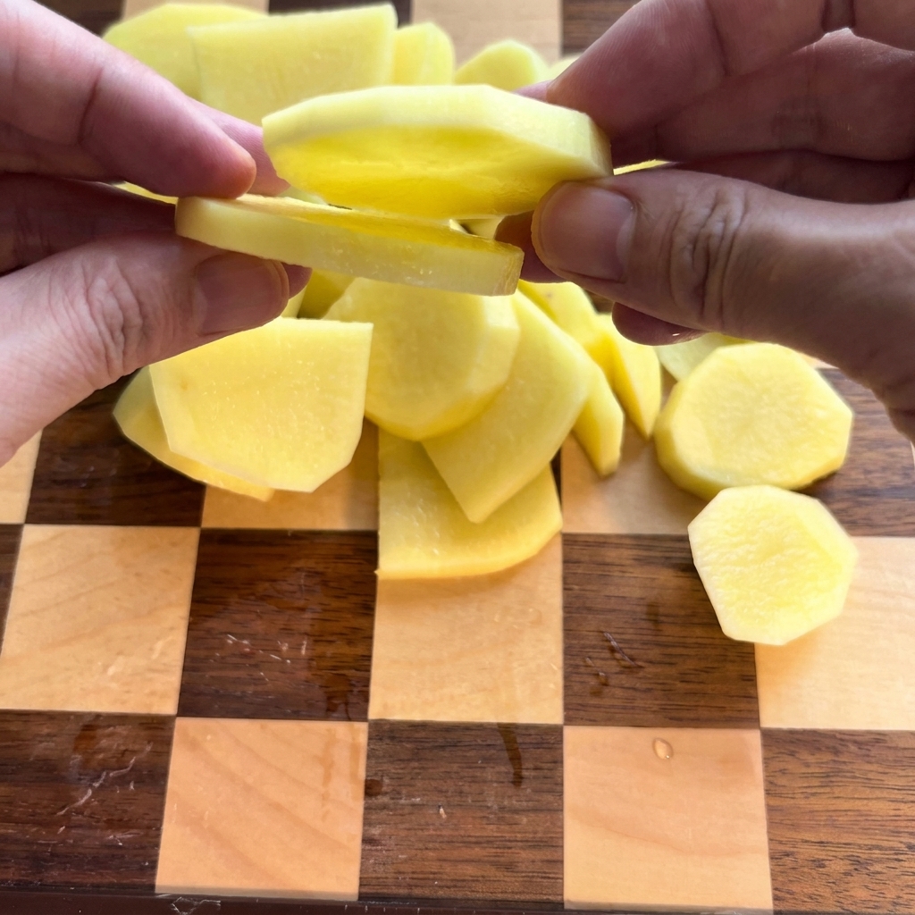 Des pommes de terre épluchées soigneusement coupées en rondelles sur une planche à découper en bois.